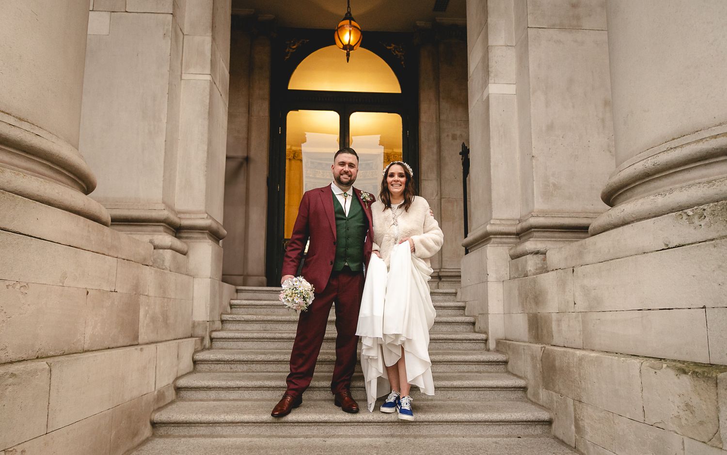 Bride and groom standing on stone steps outside a grand neoclassical building after their wedding ceremony.