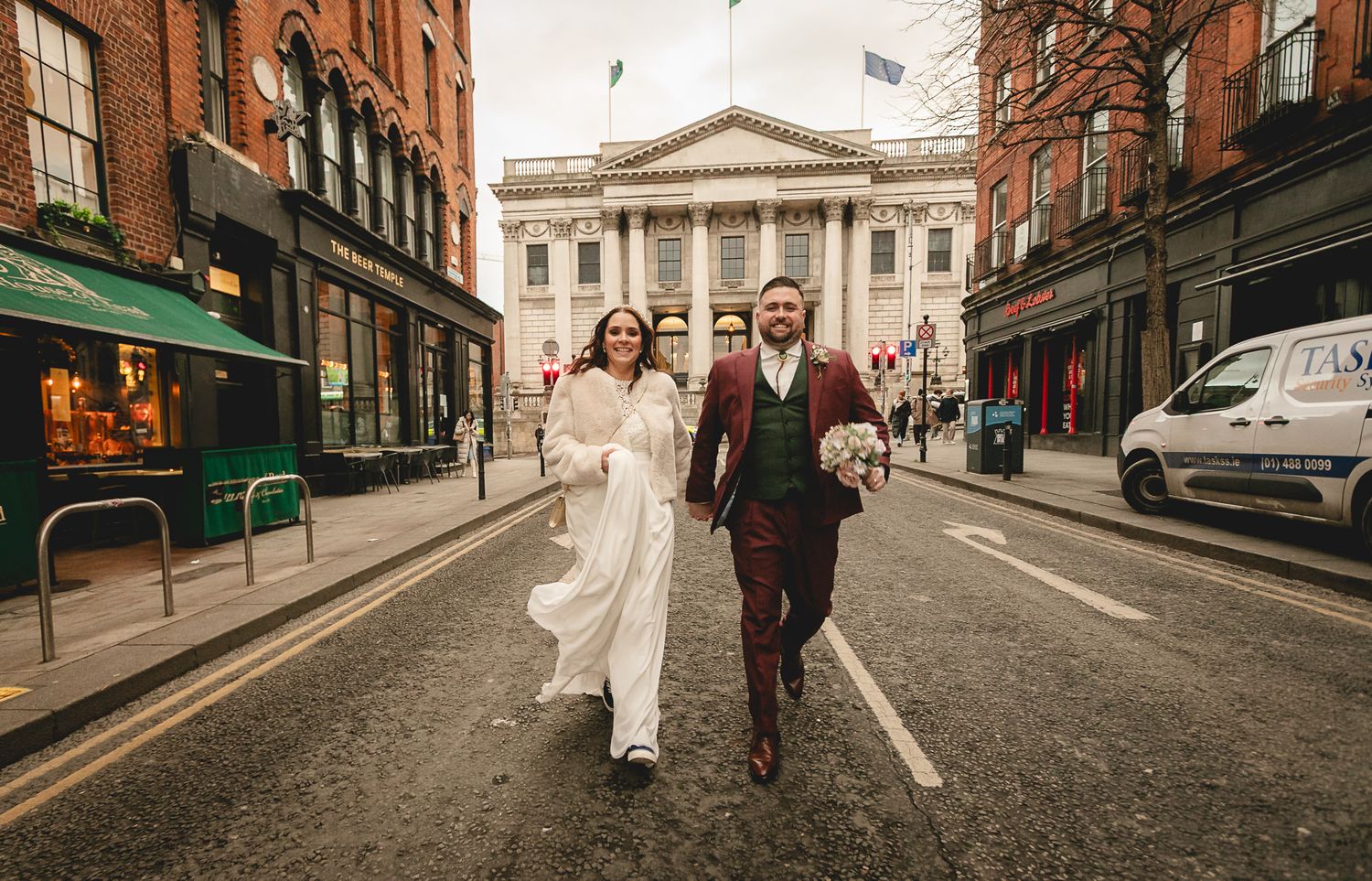 Bride, groom, and guest walking down the middle of a Dublin city street after their wedding ceremony.