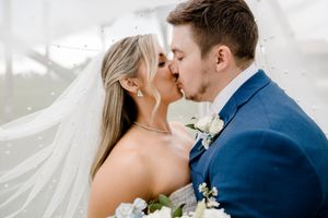 Bride and groom share a romantic kiss while her long veil flows elegantly in the wind.