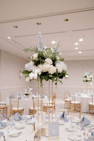 Wedding reception tables set with elegant white floral centerpieces, crystal decor, and light blue accents in a bright venue.