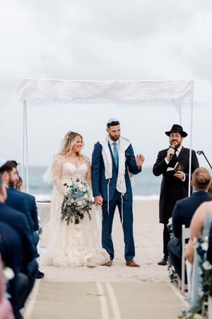 A wedding ceremony set on an elegant waterfront deck with people gathered under white drapery on a misty day.