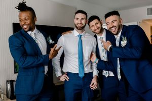 A group of groomsmen in navy blue suits share laughs while posing together at a wedding celebration.
