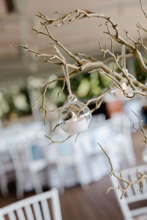 Delicate white branch decorations and crystal accents hang from the ceiling at an elegant indoor wedding reception.