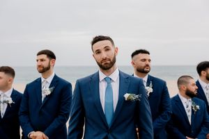 Groomsmen in navy blue suits stand in a line outdoors against a scenic mountain backdrop.