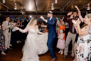 Wedding guests dance and celebrate together in a dimly lit reception venue during joyful evening festivities.