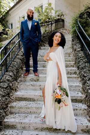 A couple celebrating their wedding poses on rustic stone steps surrounded by greenery and charm.