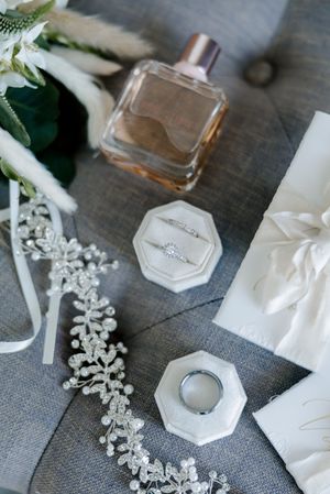 Elegant wedding accessories including hexagonal holders, perfume bottles, and delicate white floral hairpieces on gray fabric.