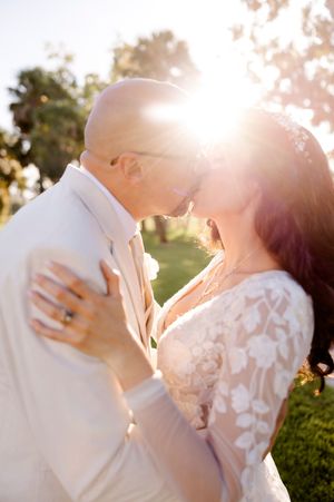 A romantic backlit wedding couple shares a kiss during golden hour in an outdoor garden setting.