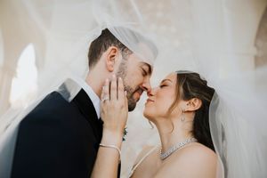 A romantic wedding couple shares a tender kiss under a flowing white veil.