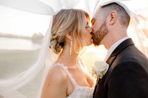 A couple shares a romantic kiss at sunset with warm golden light illuminating their wedding day moment.