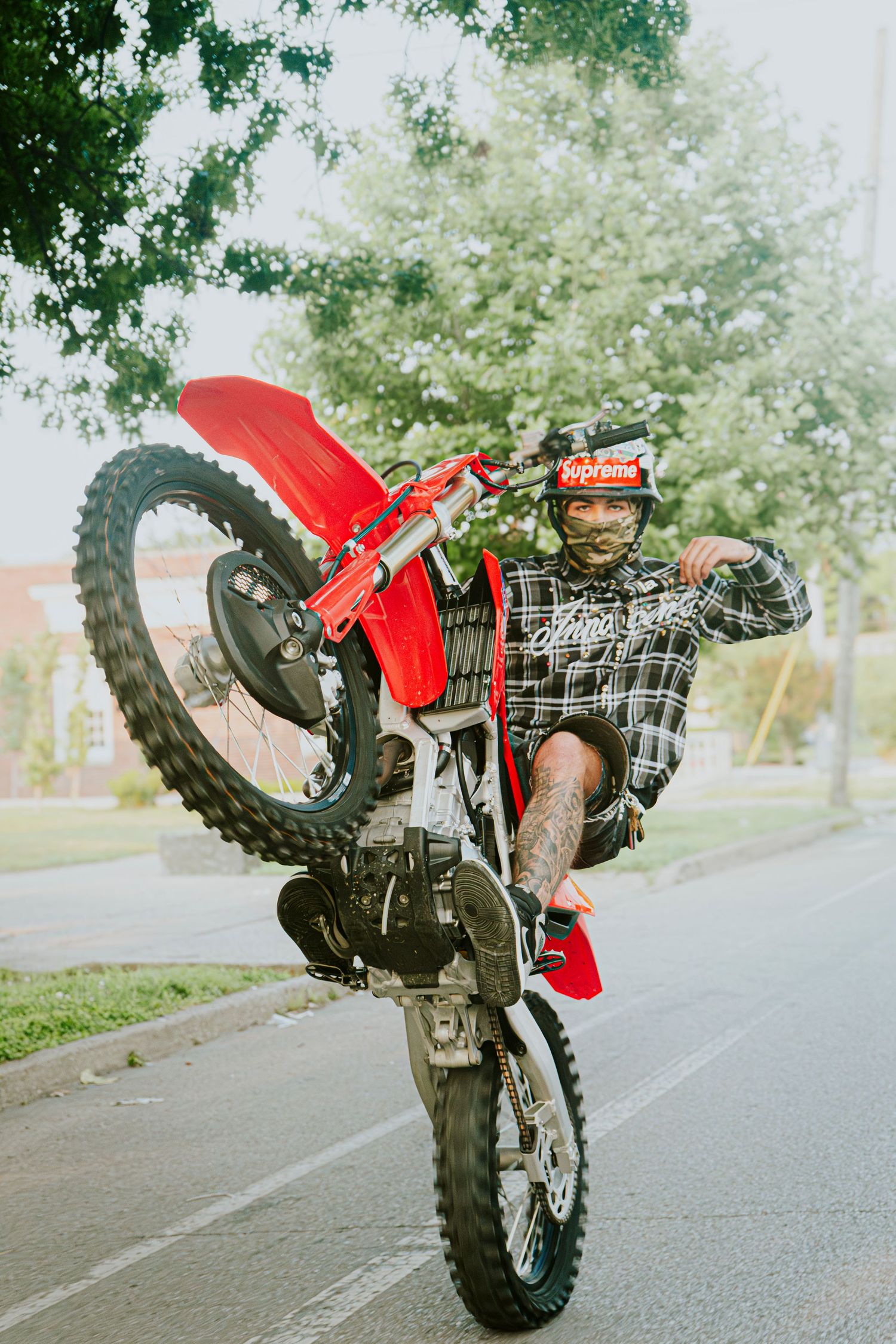 Motorcyclist performing wheelie on red dirt bike in outdoor setting.