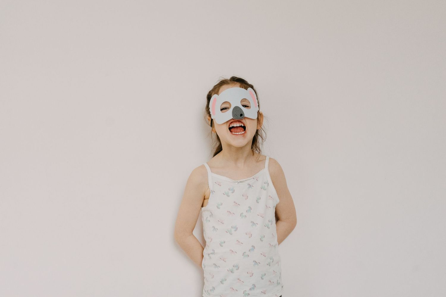 A young woman with a playful expression and paper heart-shaped glasses stands against a plain white wall.
