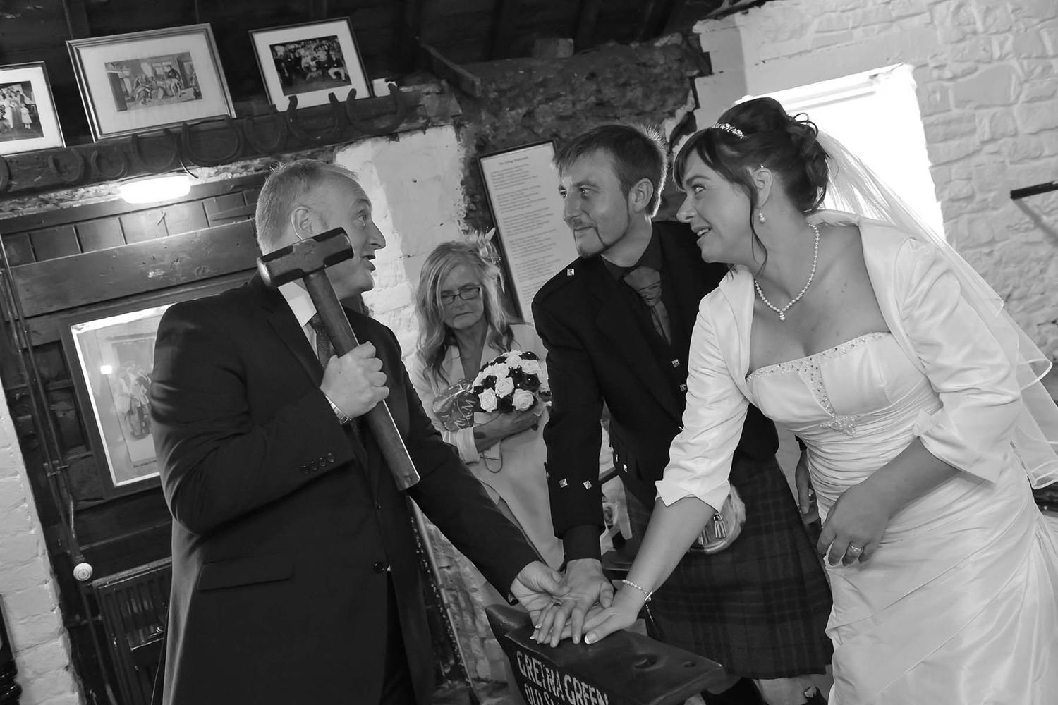 A black and white photo of a wedding ceremony, with the bride and groom standing at the old anvil in Gretna green wedding elopement