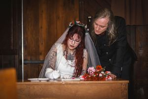 Bride and groom sign wedding documents at wooden table adorned with colorful floral bouquet.