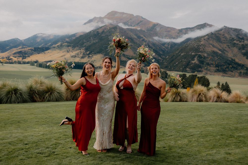 Wedding party in burgundy dresses poses against scenic mountain backdrop at outdoor celebration at Lookout Lodge Wanaka, New Zealand.