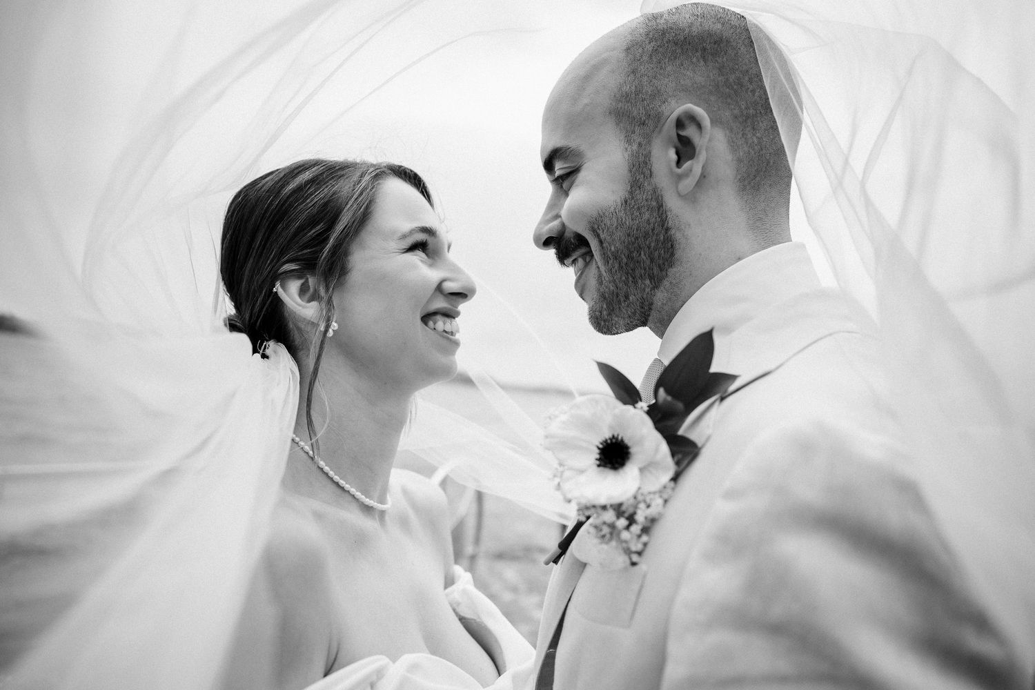 A romantic black and white wedding photo series showing tender moments between newlyweds under a flowing veil.