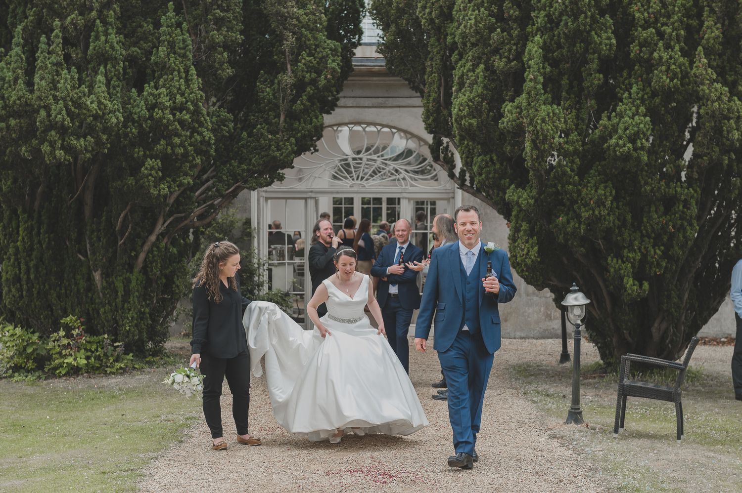 Wedding party walks along a tree-lined path during an outdoor ceremony celebration.