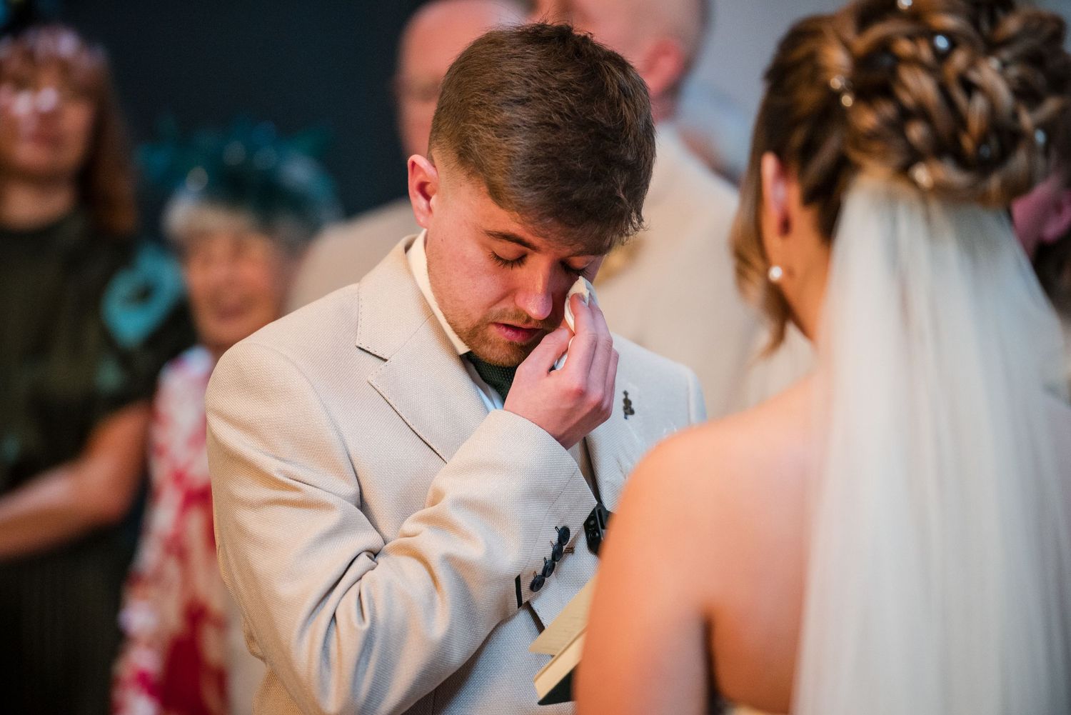 An emotional moment captured during a wedding ceremony as a person in a light beige suit wipes away tears.