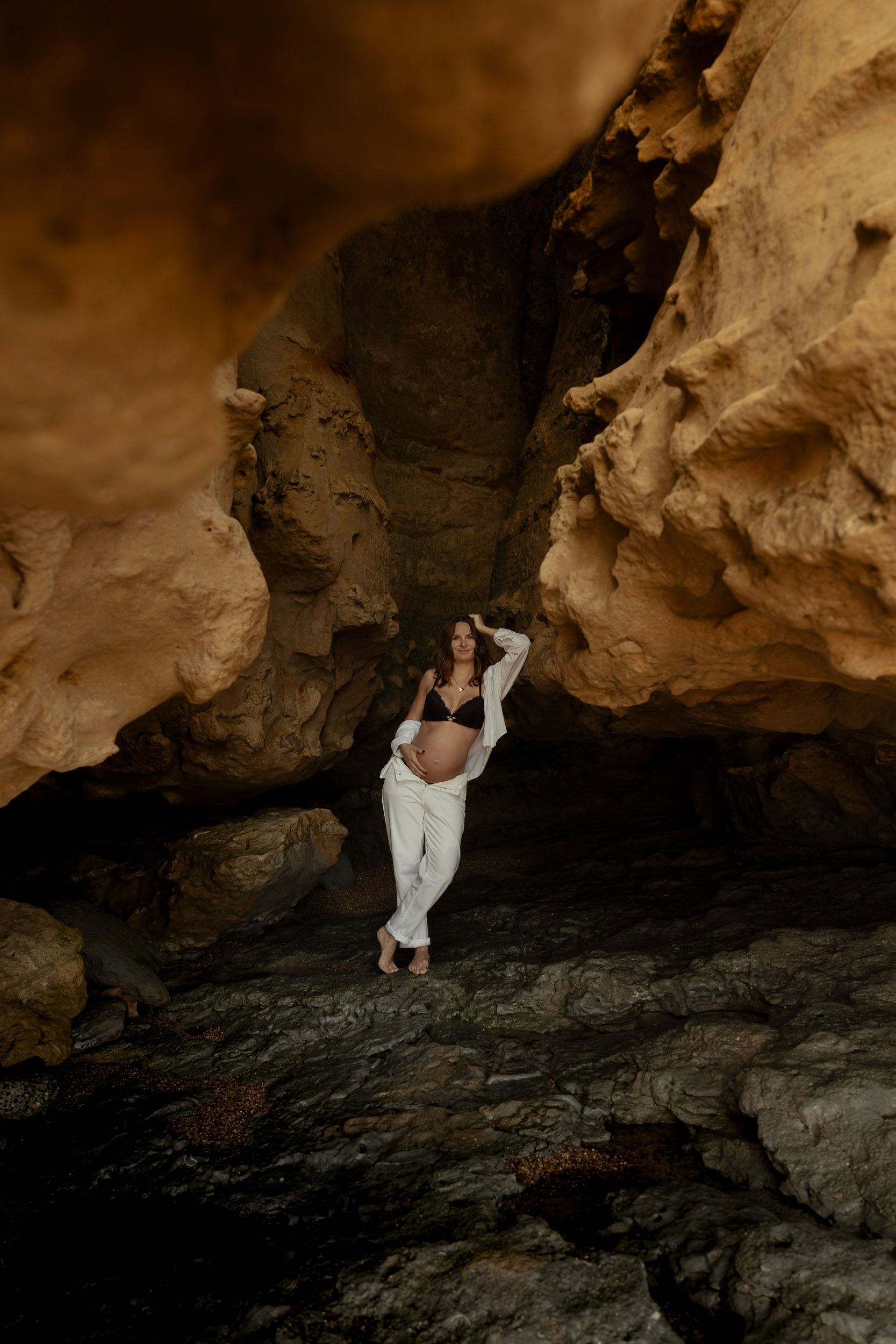 A couple explores a dramatic rocky cave formation in warm lighting.