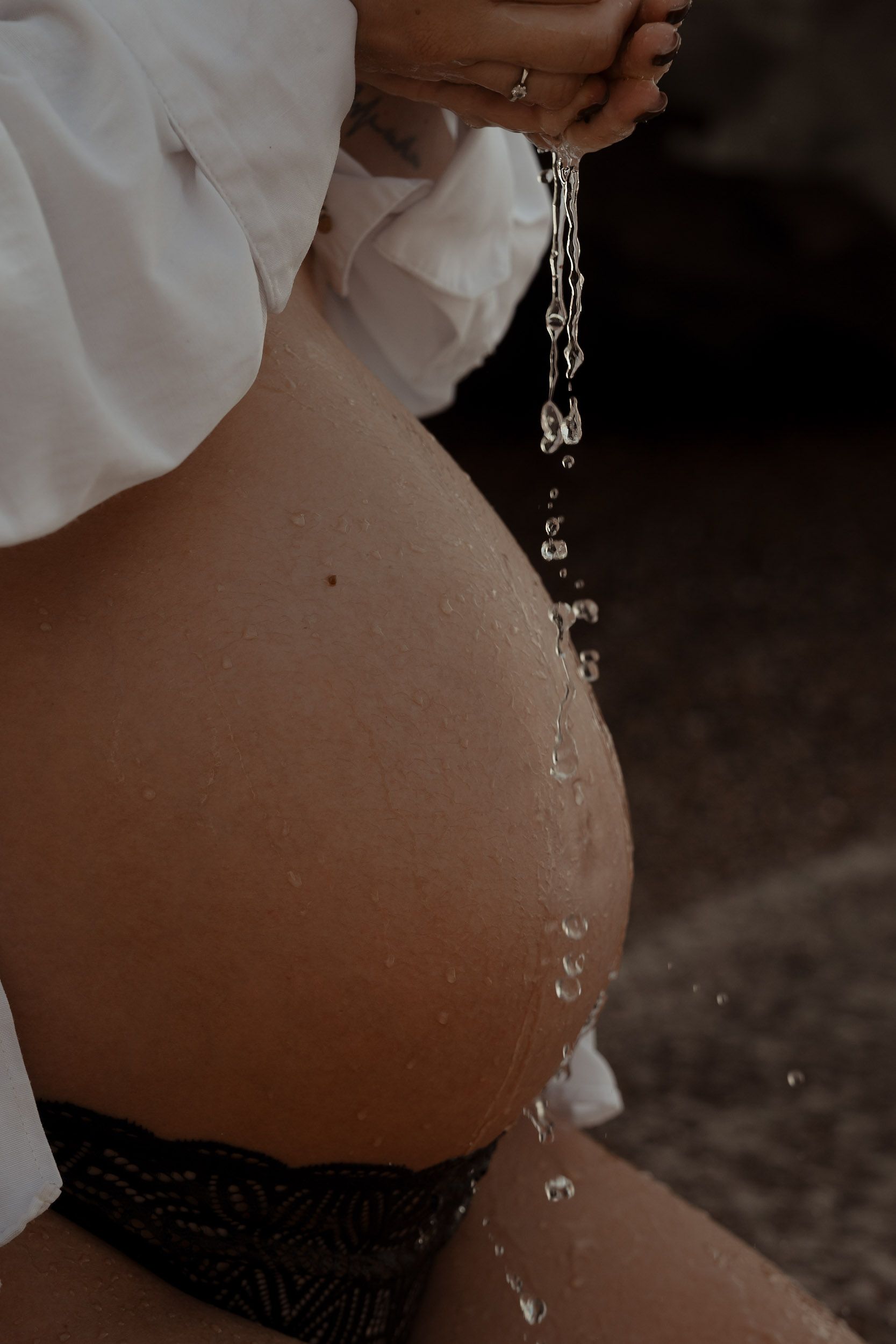 Water droplets cascade down a pregnant belly in artistic lighting.