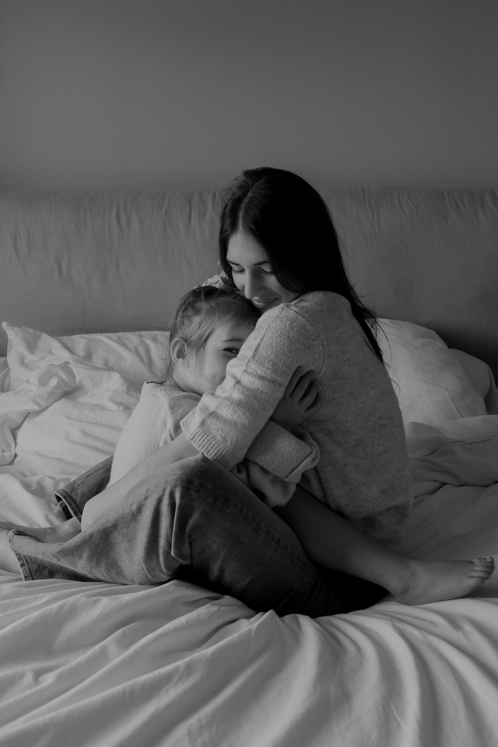 Intimate black and white photo of figures resting together on white bedding.