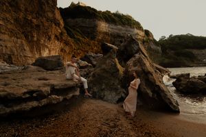 Couple walking along a dramatic rocky beach coastline during golden hour.