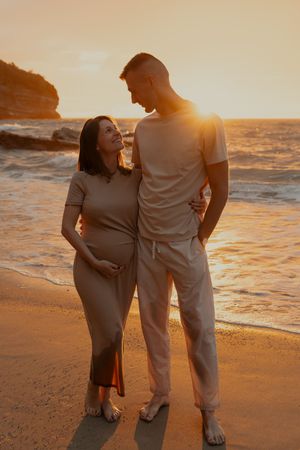 Couple embracing on sandy beach during golden sunset with waves crashing behind them.