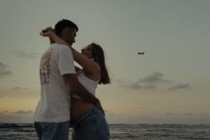 A couple embraces on a beach during golden hour with waves crashing in the background.