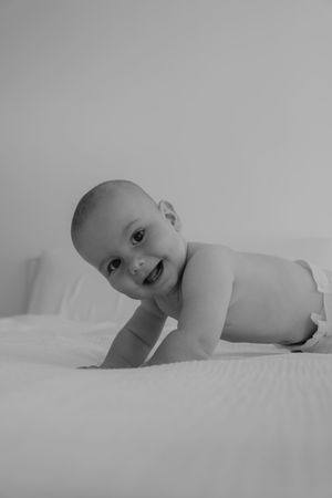 A black and white portrait of a baby lying on white bedding.