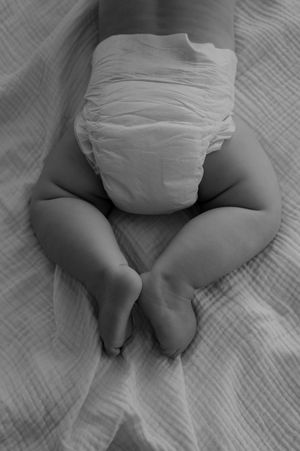 Close-up view of a baby wearing a white diaper lying on textured fabric.
