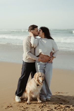 A couple shares a tender moment on the beach with their golden retriever by their side.