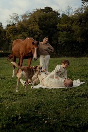 A couple relaxes on a picnic blanket in a grassy field with horses grazing nearby.