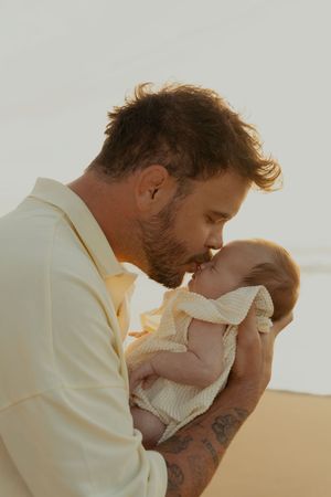 Father holding baby tenderly during sunset on beach.
