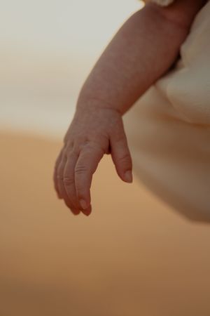 Close-up of tiny baby hand against blurred background at sunset.