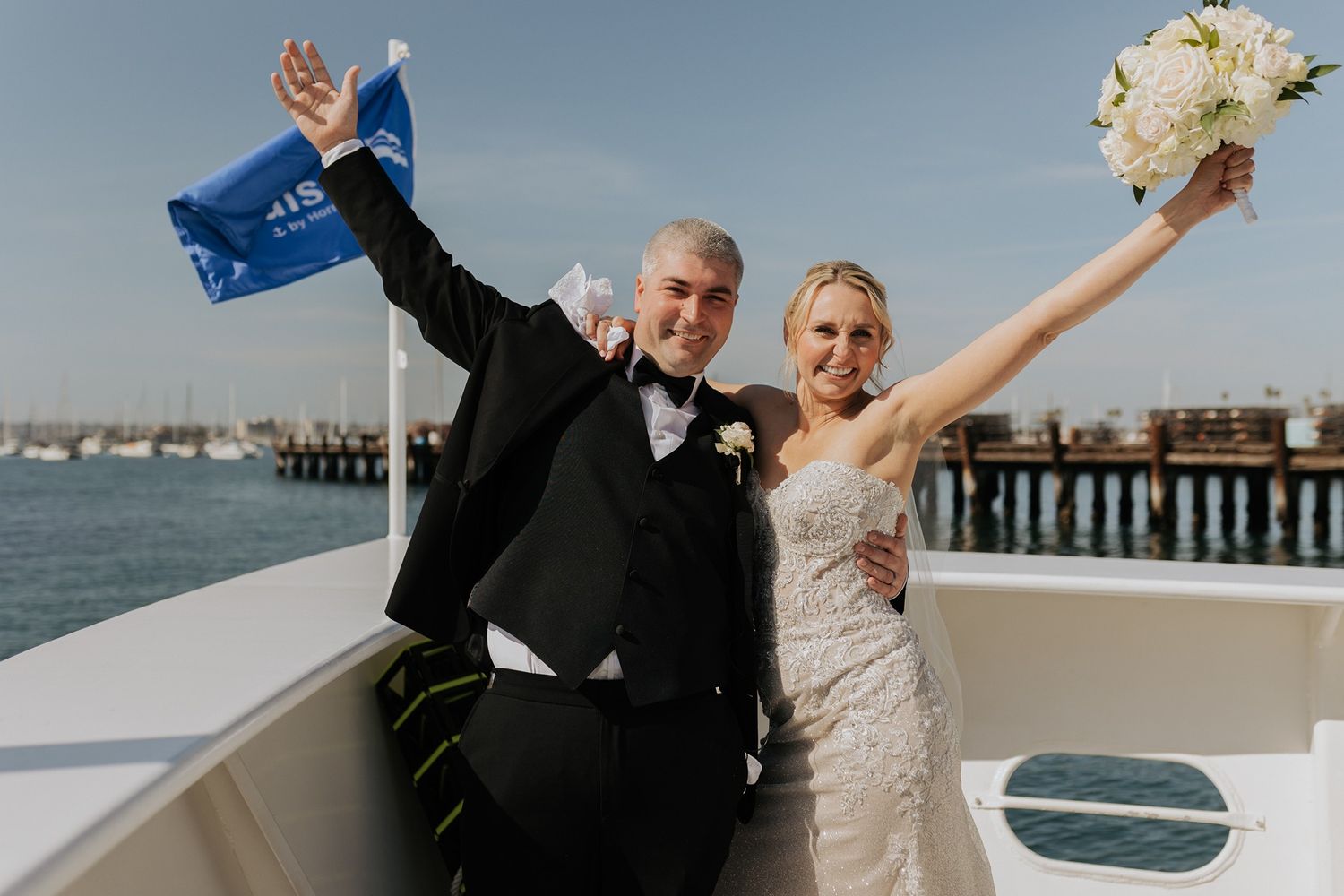 Romantic wedding couple cheers on on a boat in San Diego with ocean waves in the background.