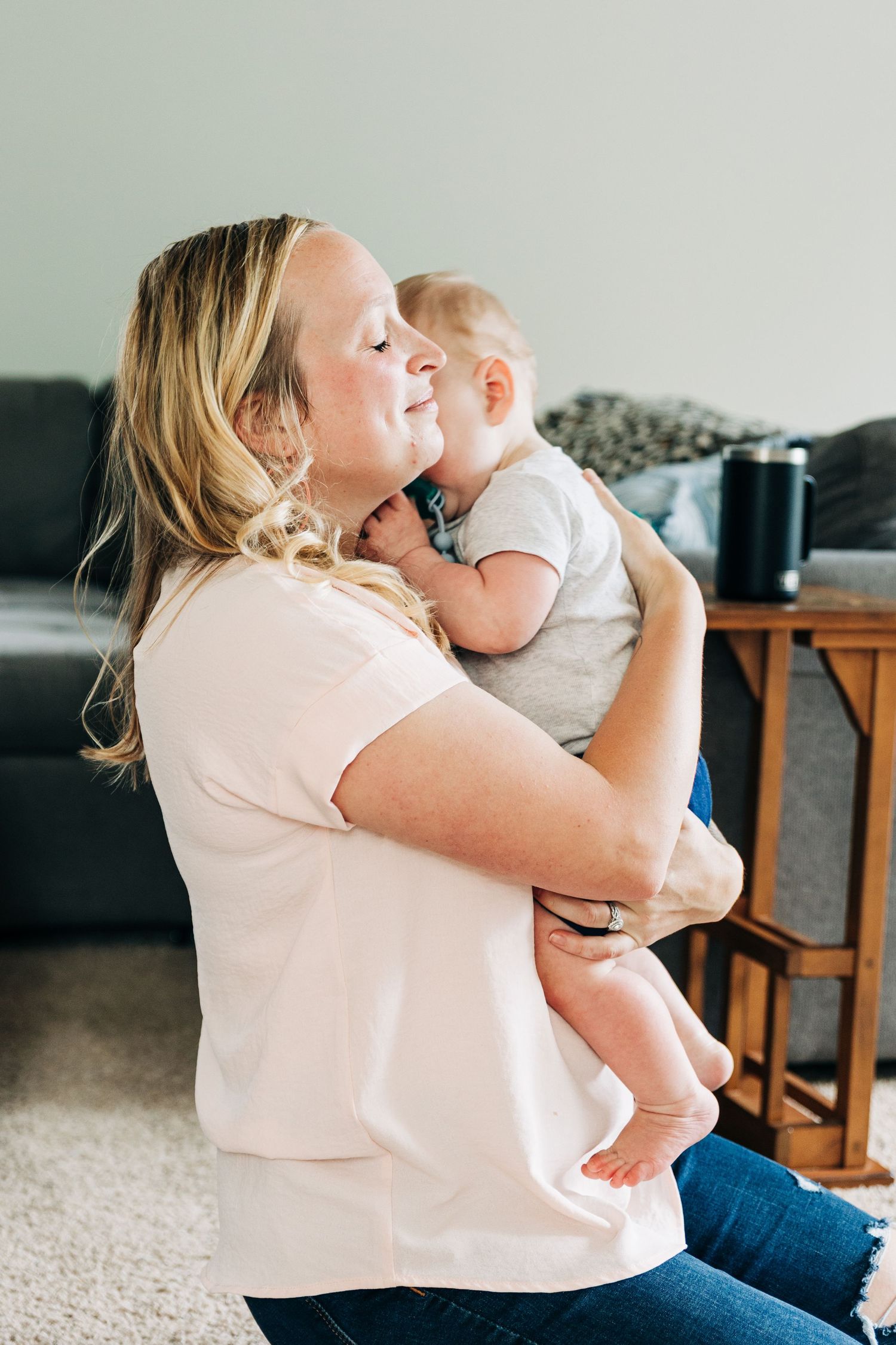 A series of candid moments showing a parent in a pink shirt holding and cuddling with a small baby on a carpeted floor.