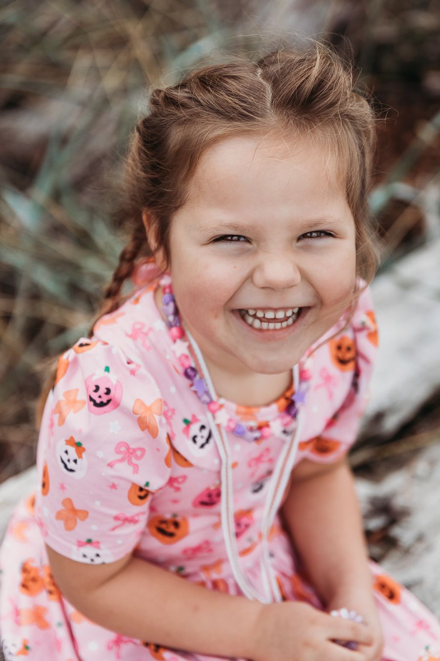 A child wearing a pink patterned dress smiles while playing outdoors.