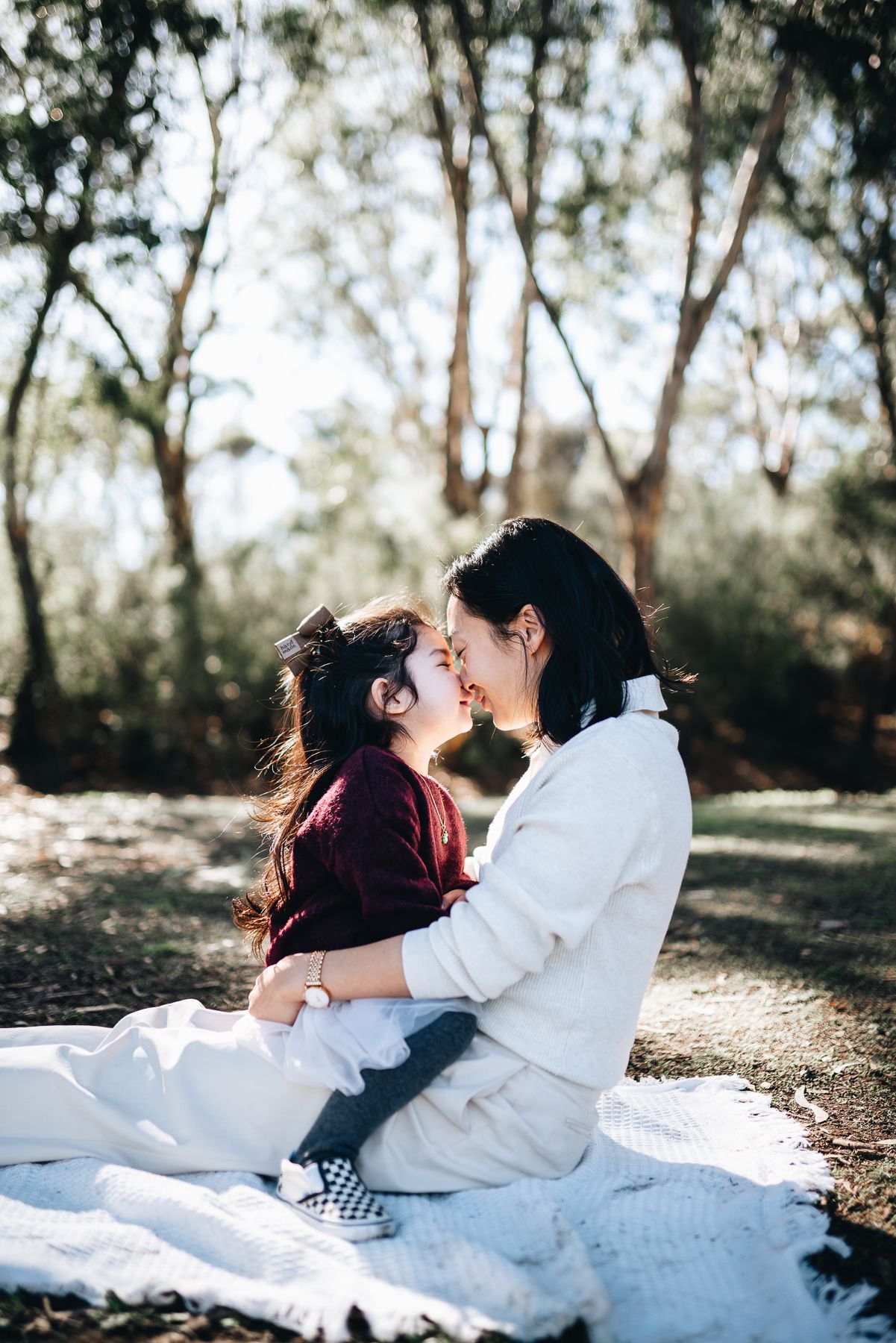 Mother and daughter shares tender moments in a sunlit outdoor setting during a Mother's Day mini session photoshoot.