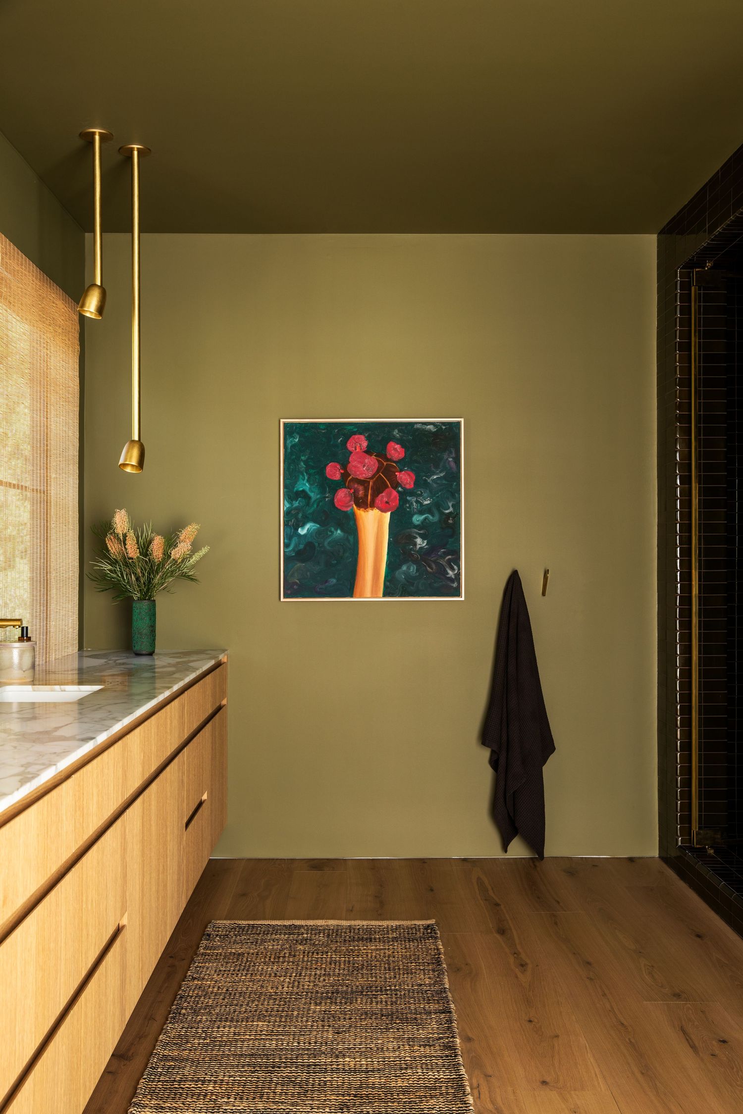 Modern bathroom interior with wooden vanity, green walls, pendant lights and colorful artwork displayed above.
