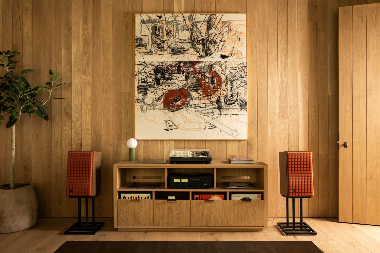 A minimalist wood-paneled room with vintage speakers, wall art, and media storage against a warm-toned backdrop.