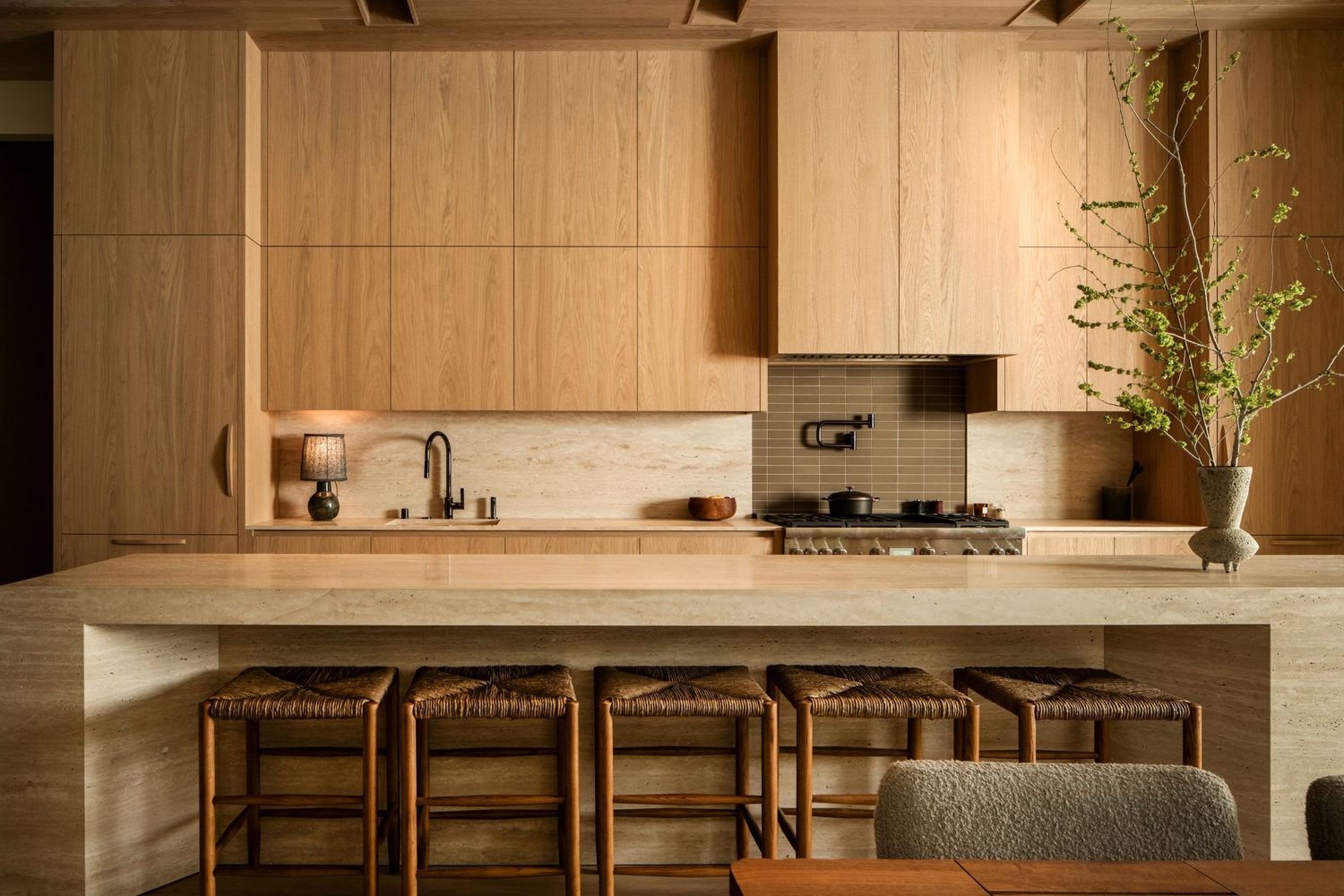 Modern minimalist kitchen interior with wooden cabinets, stone countertops and sleek appliances in warm neutral tones.