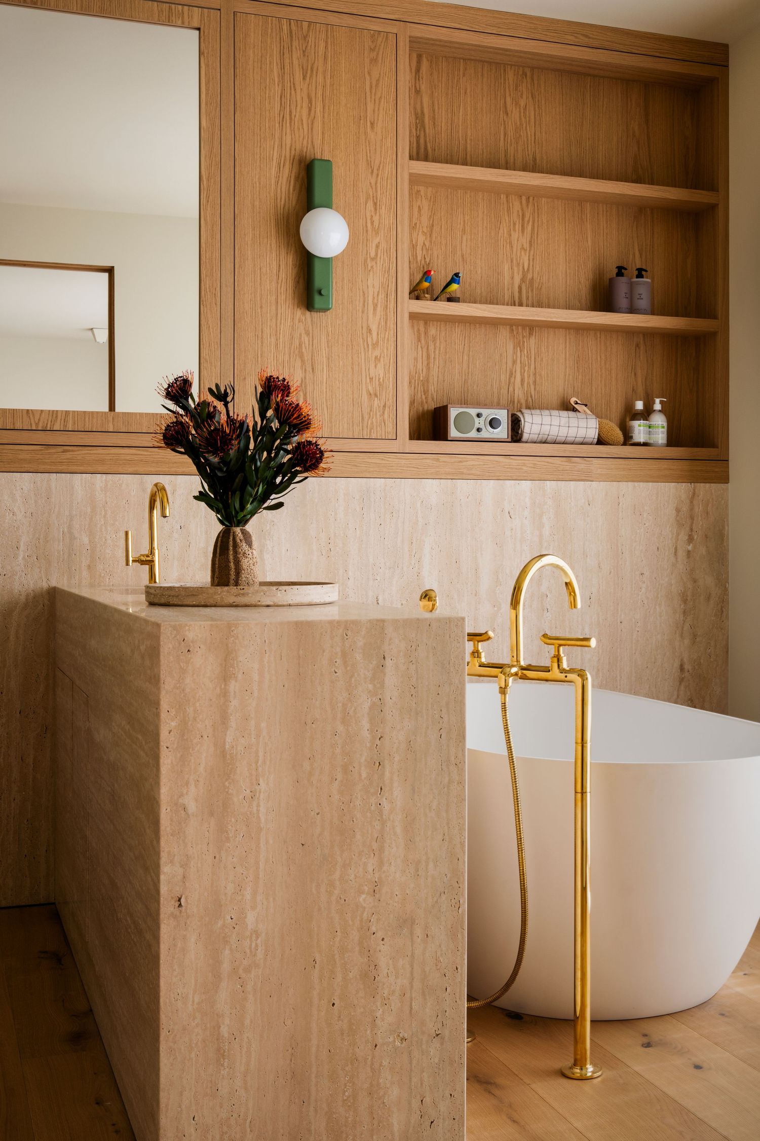 Modern bathroom interior with wooden walls, built-in shelving, and gold freestanding tub faucet fixture.
