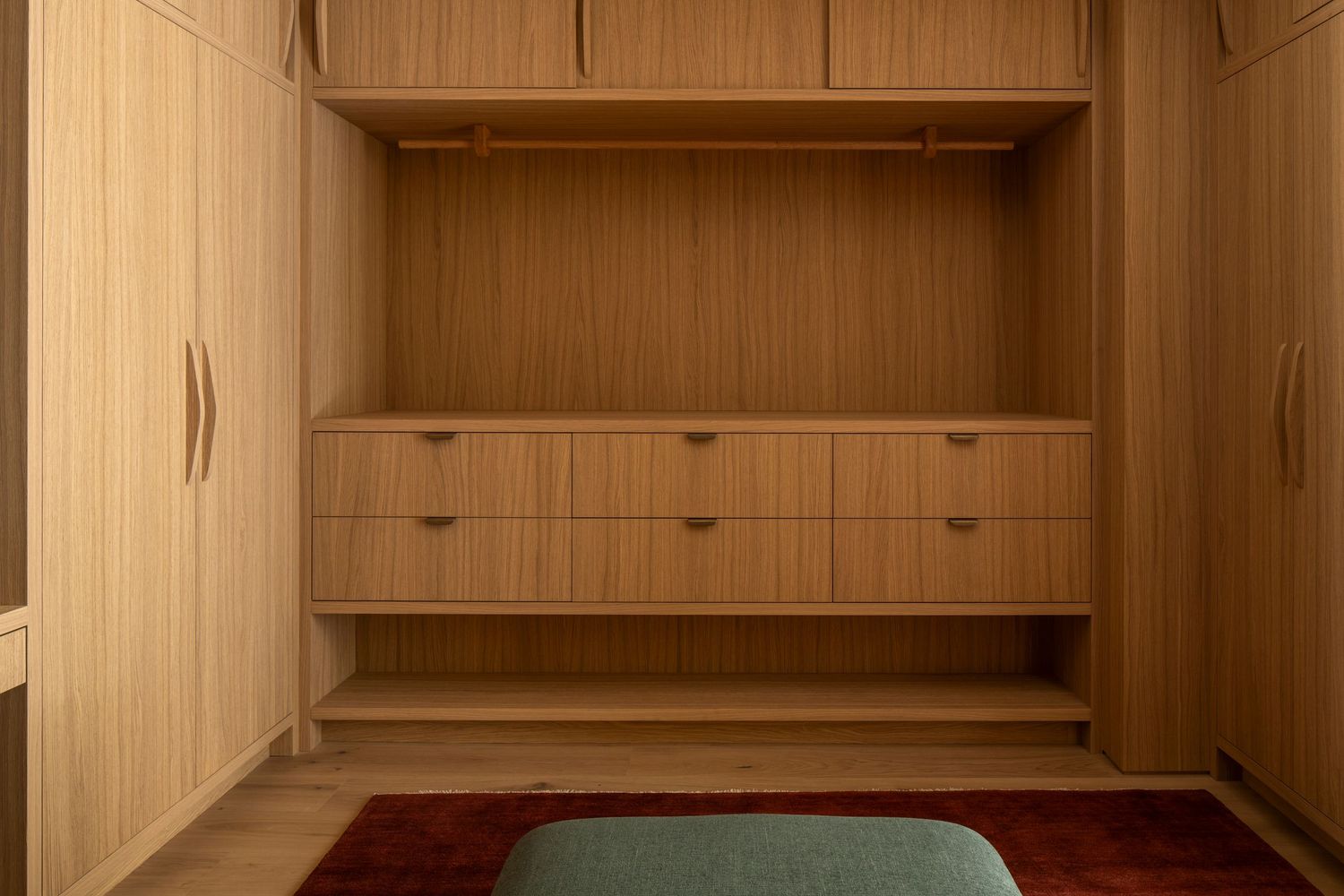 Empty wooden closet with built-in shelves and hanging rod mounted on beige wall.