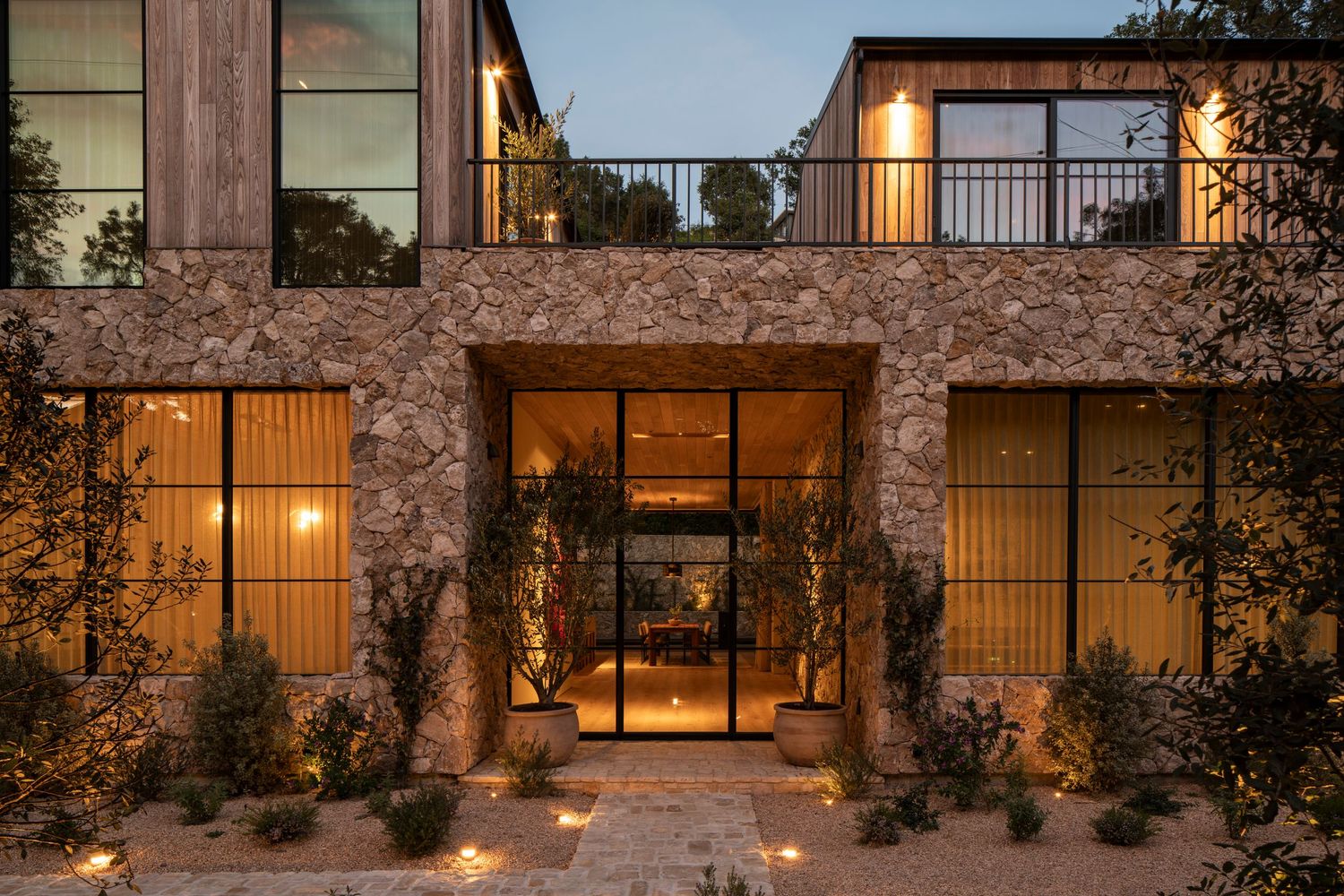 Modern stone facade luxury home entrance with warm lighting and glass doors at dusk.