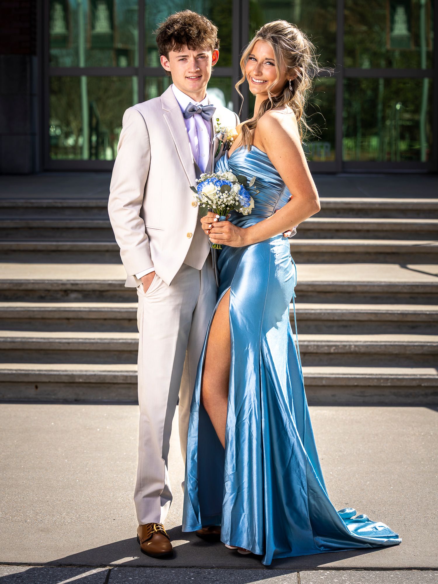 A young couple dressed formally for a special occasion, the woman wearing a long blue gown and the man in a light-colored suit.