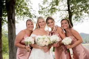Bride in white lace gown poses with three bridesmaids in pink satin dresses holding white bouquets.