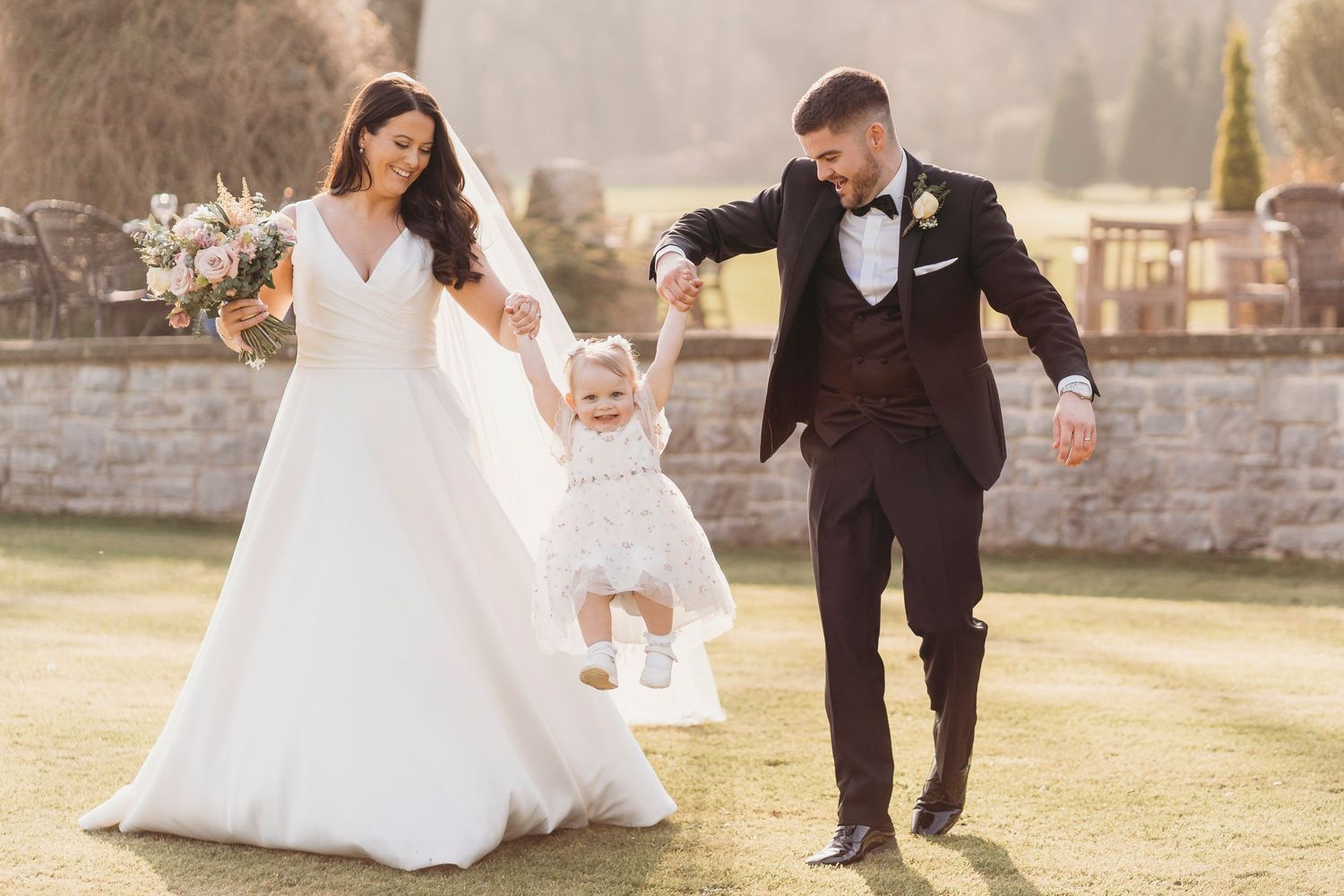 Bride and groom lifting flower girl during relaxed family wedding moment at West Wales venue