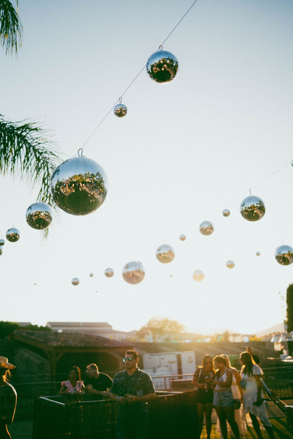 festival photos Boules disco argentées accrochées à des ficelles à l'extérieur au coucher du soleil avec des gens rassemblés en dessous