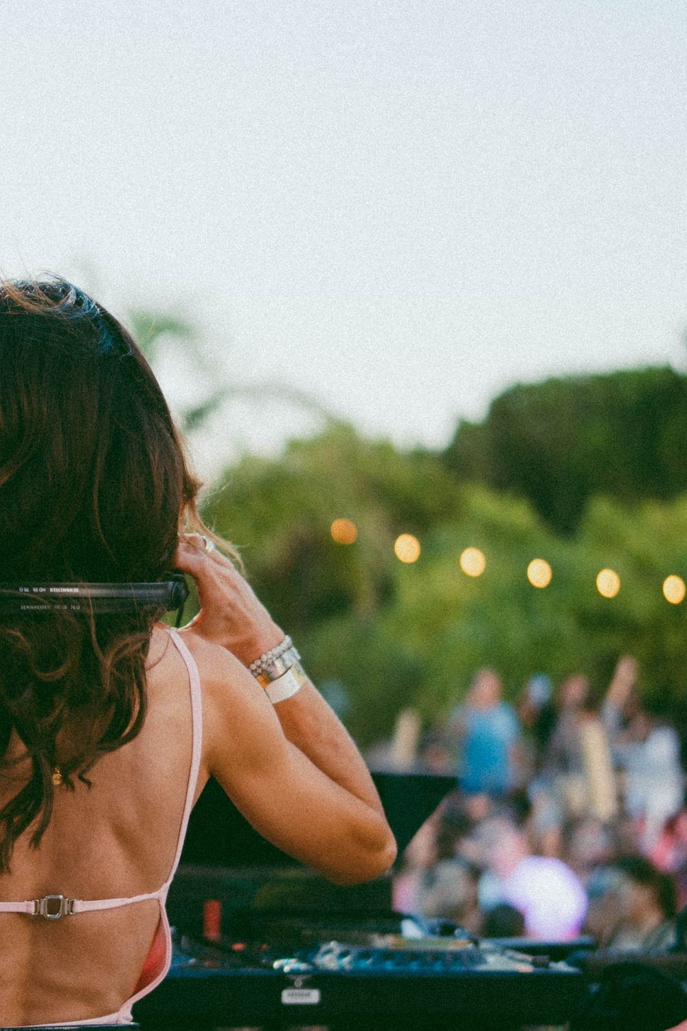DJ féminine se produisant lors d'une fête en plein air avec des guirlandes lumineuses et une foule en arrière-plan.
