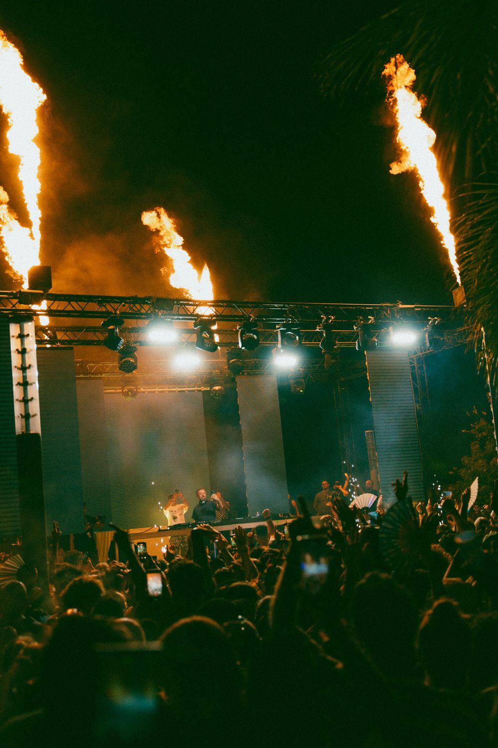 Outdoor concert stage with dramatic fire jets and crowd at night music festival.